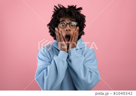 Young black teen guy touching his face, opening his mouth in shock on pink studio background Young black teen guy touching his face, opening his mouth in shock on pink studio background 81040342
