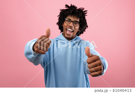 Funky Afro teen guy in glasses showing thumbs up with both hands, recommending something on pink background Funky Afro teen guy in glasses showing thumbs up with both hands, recommending something on pink background 81040413