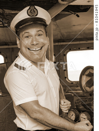 The funny captain standing in the wheelhouse of ship and looking to camera, sepia color. 81041945