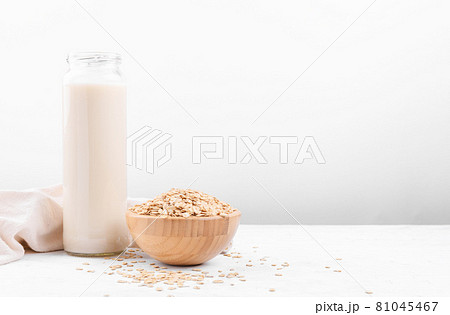 Oat milk in a bottle and a bowl with oat flake on white table Oat milk in a bottle and a bowl with oat flake on white table 81045467