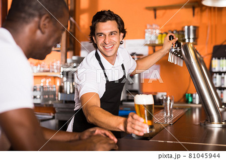 Positive man bartender giving glass of golden beer to man client 81045944