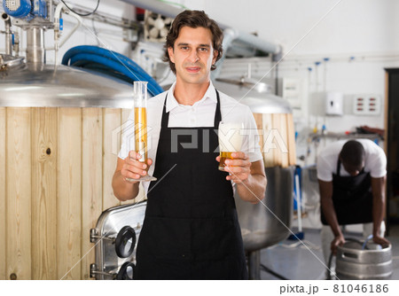 Man brewer in uniform is standing with glass of beer and flask Man brewer in uniform is standing with glass of beer and flask 81046186