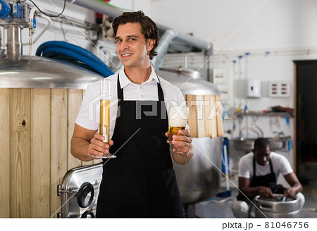 Man brewer in uniform is standing with glass of beer and flask Man brewer in uniform is standing with glass of beer and flask 81046756
