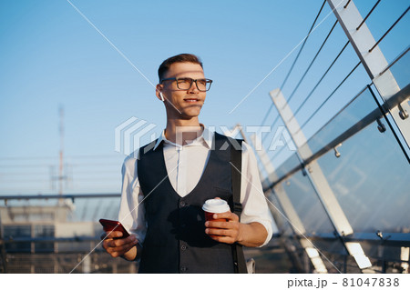 businessman with a smartphone drinks coffee on the office terrac 81047838