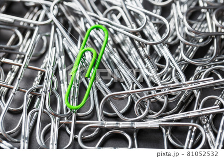 The green paper clip stands out against a textured background of silver paper clips The green paper clip stands out against a textured background of silver paper clips 81052532