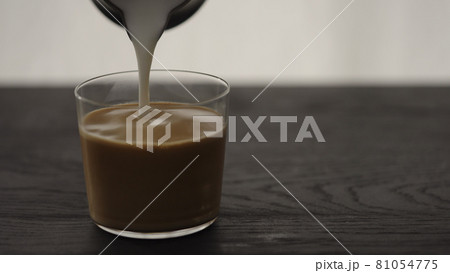 Pour steamed milk into espresso in tumbler glass on oak table with copy space Pour steamed milk into espresso in tumbler glass on oak table with copy space 81054775