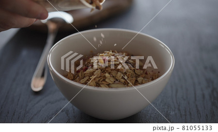 Pour granola over yogurt in white bowl 81055133