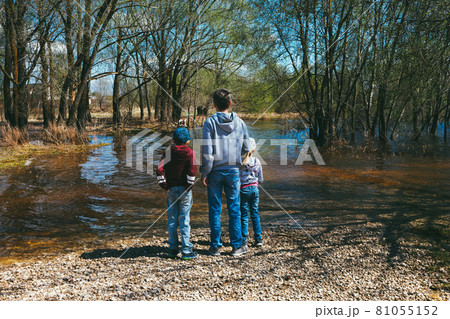 a man with his daughter and son are standing by the flooded river on a rocky beach 81055152