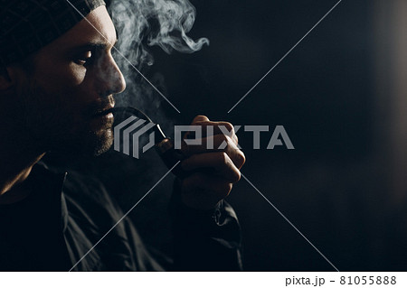 Man smoking a pipe on dark background. Back lit profile portrait. 81055888