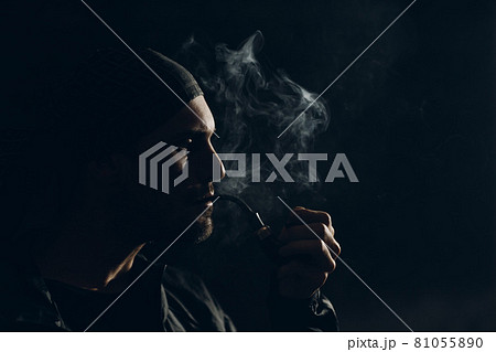 Man smoking a pipe on dark background. Back lit profile portrait. 81055890