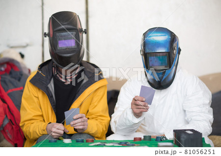 Two welders in welding masks play poker. Two welders in welding masks play poker. 81056251