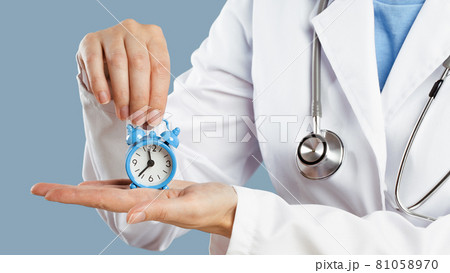Doctors hands holding an alarm clock over blue background 81058970