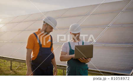 The engineer holds his hand in the air, a place for a virtual screensaver. Male engineers standing at solar farm and discussing efficient plan of construction. Two men in protective helmet. The engineer holds his hand in the air, a place for a virtual screensaver. Male engineers standing at solar farm and discussing efficient plan of construction. Two men in protective helmet. 81058972