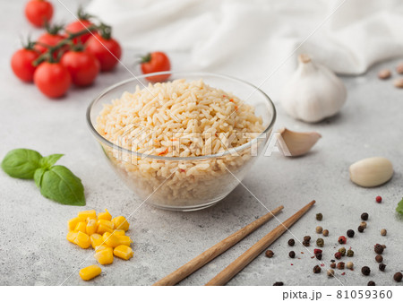 Glass bowl with boiled long grain basmati rice with vegetables on light table background with sticks 81059360