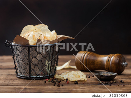 Crunchy potato crisps chips with  black pepper in steel snack bucket on wooden background with mill  81059363