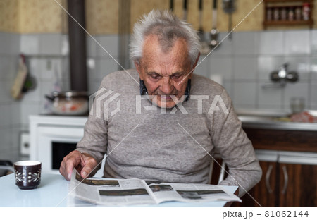 Portrait of elderly man sitting at the table indoors at home, reading newspapers. 81062144