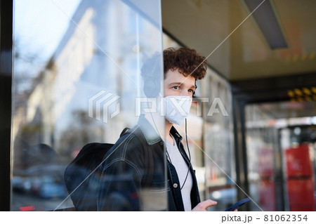 Portrait of young man commuter standing on bus stop outdoors in city, coronavirus concept. Portrait of young man commuter standing on bus stop outdoors in city, coronavirus concept. 81062354