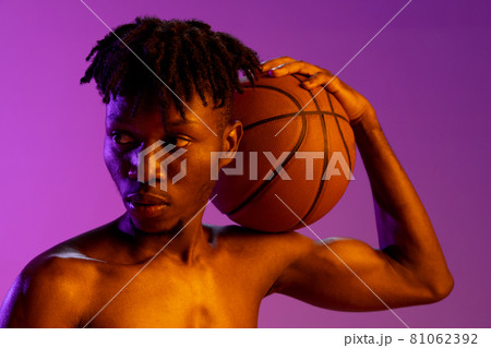 Young african man, basketball player holding ball in hands isolated over purple neon background. 81062392