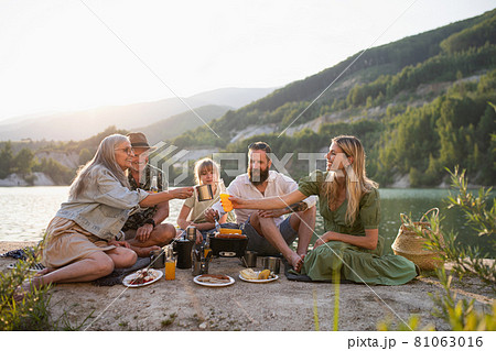 Happy multigeneration family on summer holiday trip, barbecue by lake. Happy multigeneration family on summer holiday trip, barbecue by lake. 81063016
