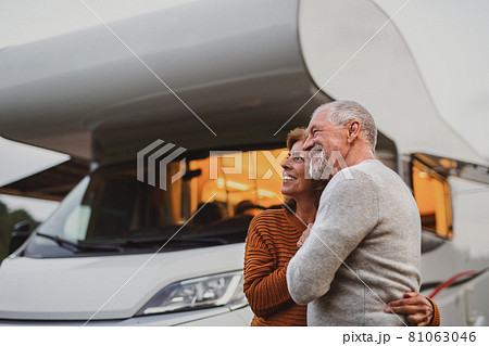 Senior couple standing and hugging outdoors at dusk, caravan holiday trip. 81063046