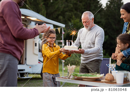 Multi-generation family celebrating birthday outdoors at campsite, caravan holiday trip. 81063048