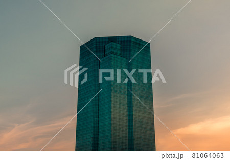 Angular geometric mirror cladding on a modern building with repeating structure and reflected sky background at evening time. Angular geometric mirror cladding on a modern building with repeating structure and reflected sky background at evening time. 81064063
