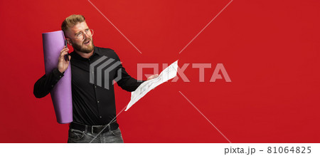 Portrait of funny bearded man, builder, designer or architect with professional equipment isolated on red studio background. 81064825