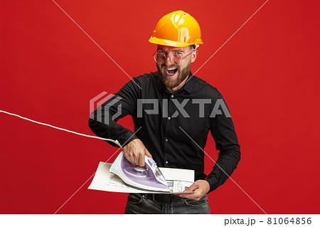 Portrait of funny bearded man, builder, designer or architect with professional equipment isolated on red studio background. Portrait of funny bearded man, builder, designer or architect with professional equipment isolated on red studio background. 81064856