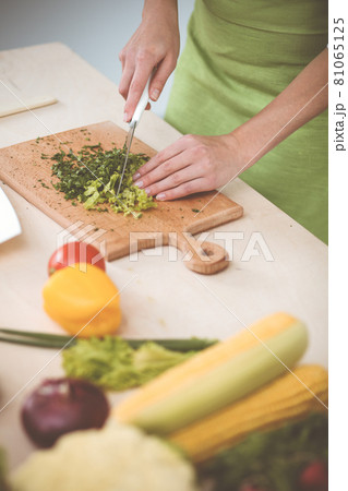 Unknown young woman slicing greens for a delicious fresh vegetarian salad while standing at the kitchen desk, just hands, close-up. Cooking concept Unknown young woman slicing greens for a delicious fresh vegetarian salad while standing at the kitchen desk, just hands, close-up. Cooking concept 81065125