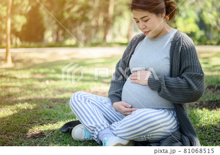 Portrait of young Asian pregnant woman holding her belly during relax in the park. Conceptual shot of healthy pregnant woman feeling. 81068515