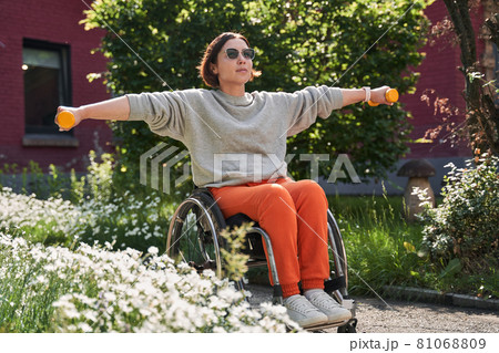 Handicapped woman holding dumbbells and training at the fresh air around the trees Handicapped woman holding dumbbells and training at the fresh air around the trees 81068809