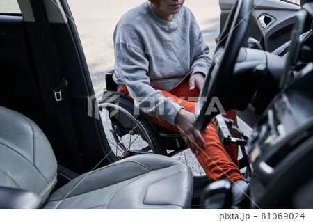 Young disabled female getting out from the car in her wheelchair after the road 81069024