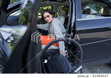 Disabled person getting out from the wheelchair in her car Disabled person getting out from the wheelchair in her car 81069047