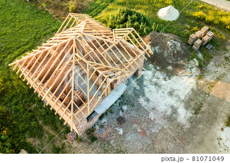 Aerial view of unfinished brick house with wooden roof structure under construction. 81071049