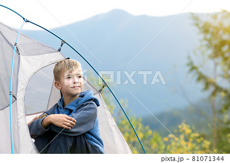 Hiker child boy sitting inside a tent in mountain campsite enjoying view of nature. 81071344