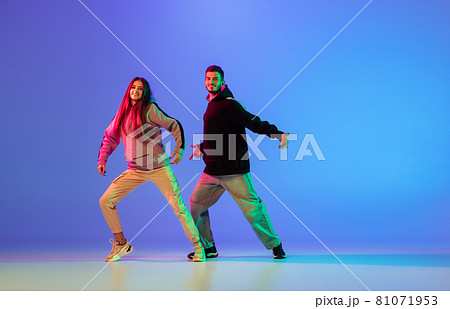 Two young people, man and woman dancing brakedance, hip-hop over blue background in neon light. Two young people, man and woman dancing brakedance, hip-hop over blue background in neon light. 81071953