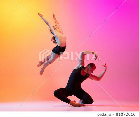 Two dancers, stylish sportive couple, male and female models dancing contemporary dance on colorful gradient yellow pink background in neon light. Two dancers, stylish sportive couple, male and female models dancing contemporary dance on colorful gradient yellow pink background in neon light. 81072616