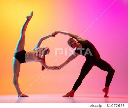 Two dancers, stylish sportive couple, male and female models dancing contemporary dance on colorful gradient yellow pink background in neon light. Two dancers, stylish sportive couple, male and female models dancing contemporary dance on colorful gradient yellow pink background in neon light. 81072623