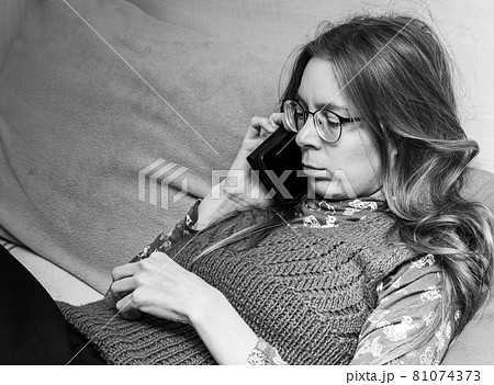 Serious sad upset young woman with long hair with smartphone in her hands is talking on the phone while sitting on couch at home. Black and white photo. Human emotions. Copy space for text. Serious sad upset young woman with long hair with smartphone in her hands is talking on the phone while sitting on couch at home. Black and white photo. Human emotions. Copy space for text. 81074373