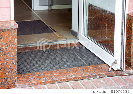open plastic entrance doors with glass with rubber foot mat close-up of building architecture with granite facade shop entry, nobody. 81076555