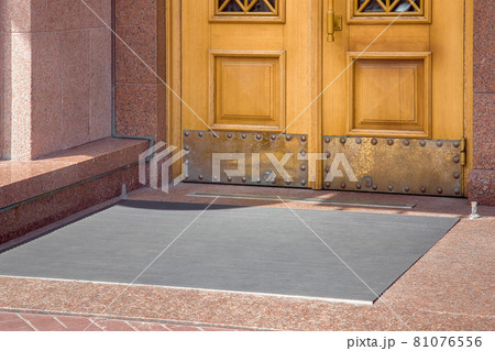 stone entrance with foot mat at the entry door made of wood and granite stone facade cladding of retro European architecture building closeup side view on sunny day, nobody. 81076556
