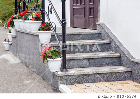 steps leading up to a threshold building of granite stairs with railing and plastic pot with floers on facade of house close up, nobody. 81076574