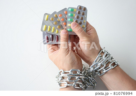 Male hands tied with chain and hold various medical pills closeup Male hands tied with chain and hold various medical pills closeup 81076994