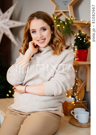 a beautiful pregnant woman sits on the table in the New Year's kitchen. a beautiful pregnant woman sits on the table in the New Year's kitchen. 81082667