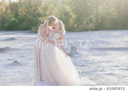 Beautiful lesbian couple walking on sand along river bank on their wedding day Beautiful lesbian couple walking on sand along river bank on their wedding day 81085653