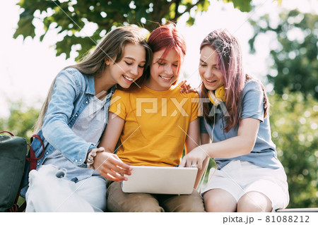 Three teenage girls communicate with their friends and classmates via video link using a laptop in the park. Friends, friendship, time together Three teenage girls communicate with their friends and classmates via video link using a laptop in the park. Friends, friendship, time together 81088212