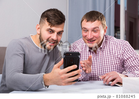 Cheerful men talking at home, using phone Cheerful men talking at home, using phone 81088245