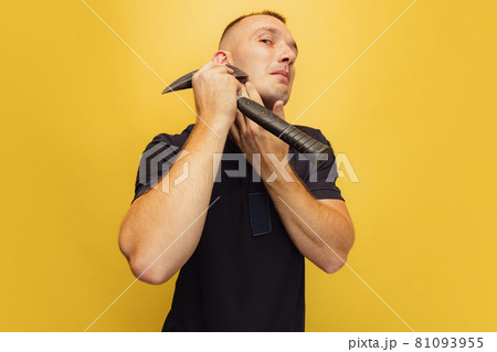 One young brutal man, firefighter shaving with an axe over yellow studio background. 81093955