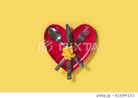 Heart shape red plate and cutlery set on yellow background Heart shape red plate and cutlery set on yellow background 81094133