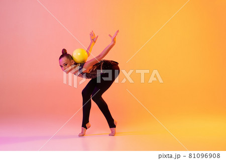 Portrait of little girl, rhythmic gymnastics artist isolated on pink yellow studio background in neon. Concept of sport, action, aspiration, education, active lifestyle 81096908